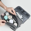 A hand is opening a gray portable waterproof toiletry washbag containing various personal care items.
