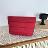 A red quilted cosmetic travel bag resting on a wooden surface next to a black candle holder.
