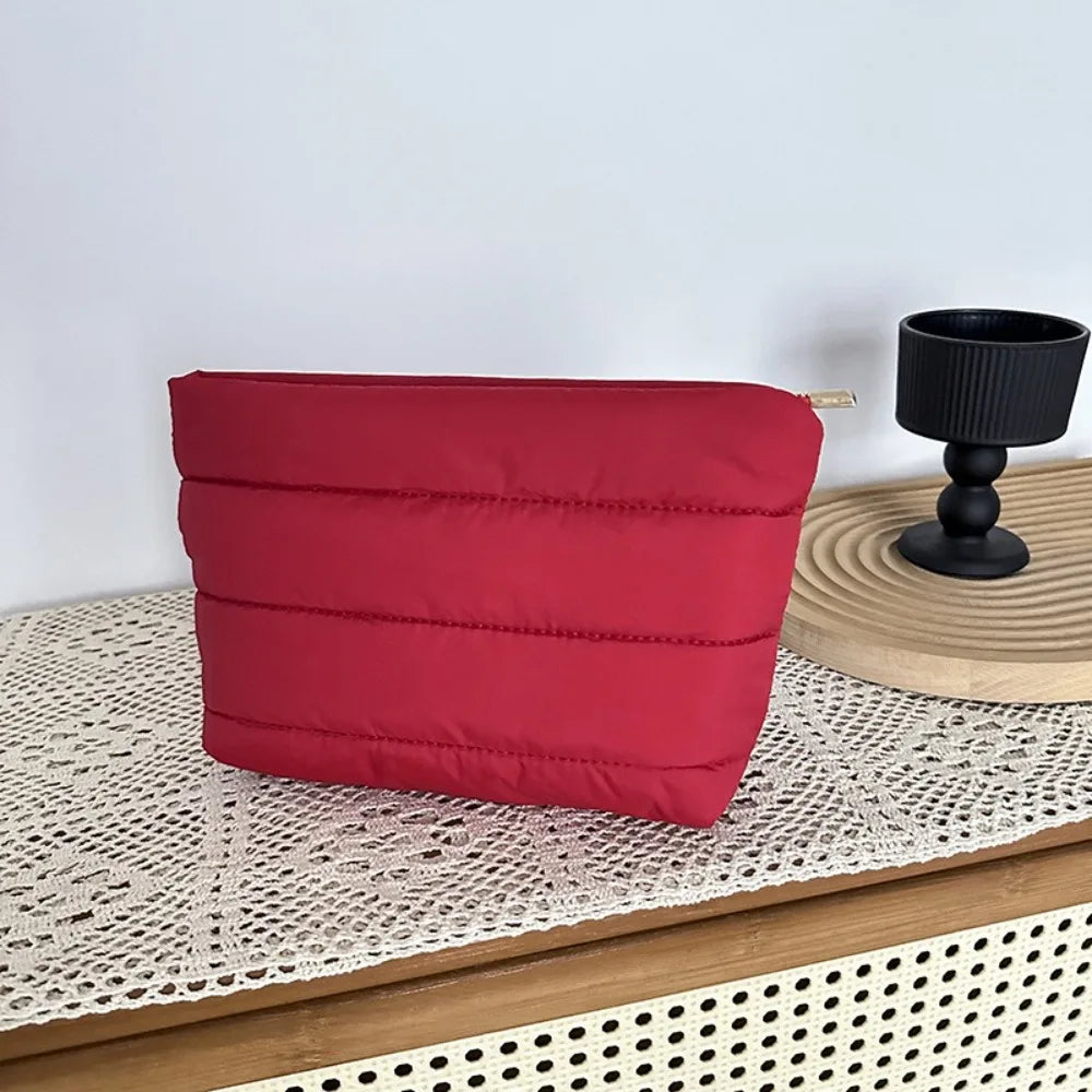 A red quilted cosmetic travel bag resting on a wooden surface next to a black candle holder.