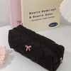 Black quilted cosmetic bag with a pink bow resting in front of a beige box labeled Beurre demi-sel & Beurre doux.