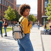 A young woman with curly hair wearing a yellow sweater and jeans carries a transparent PVC daypack while walking on a sidewal