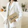 A woman holds a beige handwoven straw makeup bag with the name Your Name in it, wearing a white blazer.