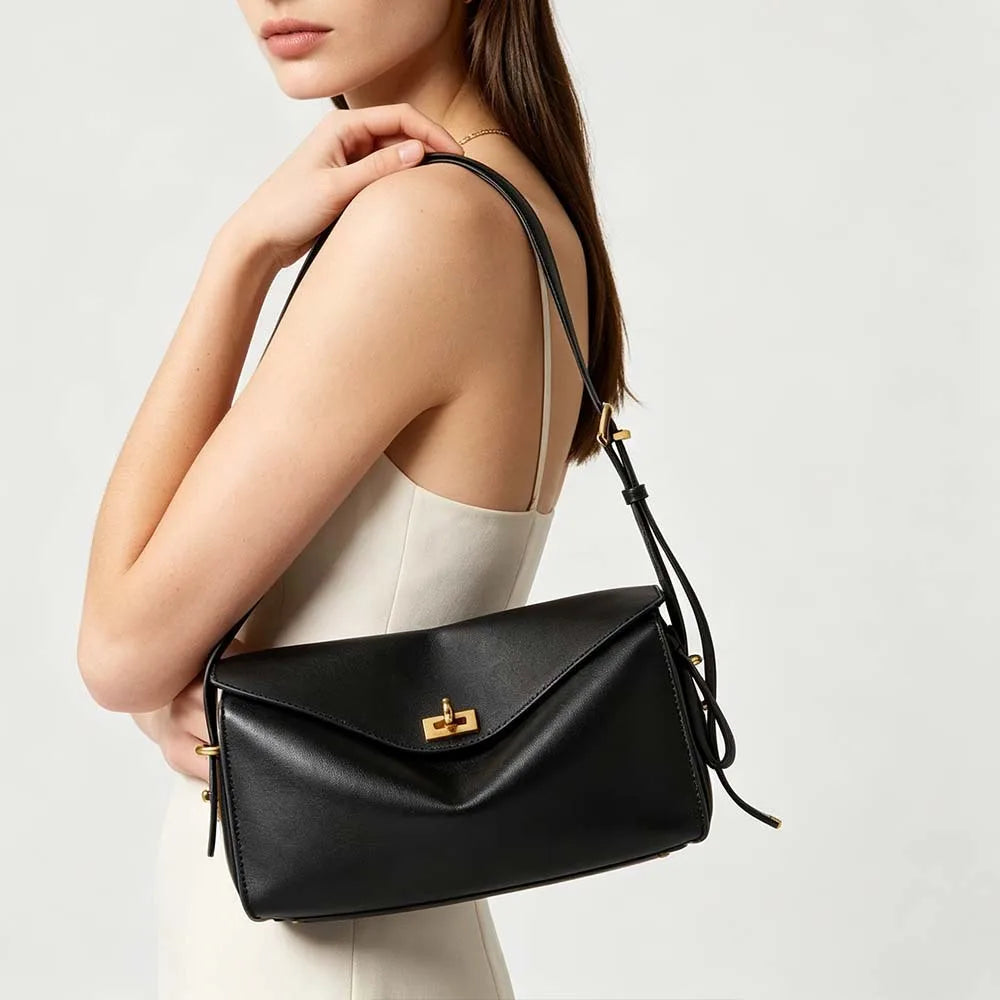 A woman holds a black genuine leather square shoulder crossbody bag with gold hardware.