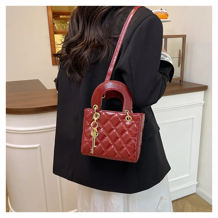 A woman holds a red quilted leather crossbody bag with gold hardware against a white fireplace mantel.