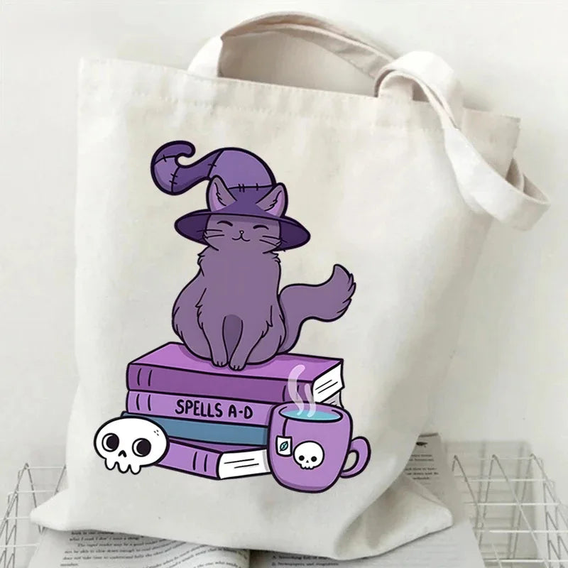 A canvas tote bag featuring a purple cat illustration sitting atop a stack of books and a teacup.