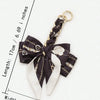 A black and white patterned bow made of fabric is attached to a gold-colored chain strap extension.