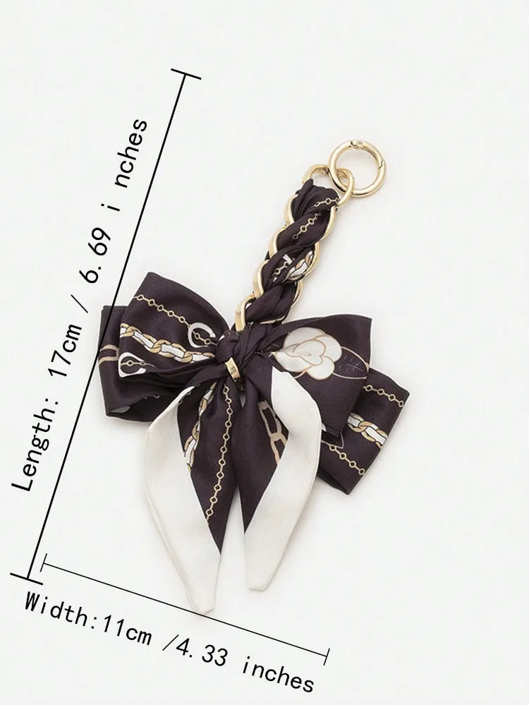 A black and white patterned bow made of fabric is attached to a gold-colored chain strap extension.