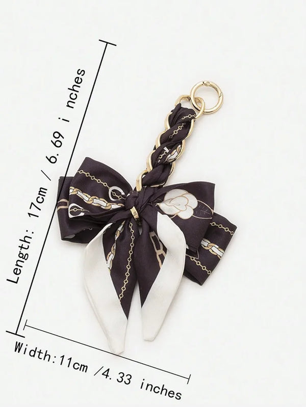 A black and white patterned bow made of fabric is attached to a gold-colored chain strap extension.