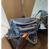 Sac bandoulière en denim délavé vintage posé sur une surface sombre à côté d'un livre.