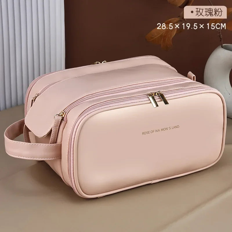 A light pink PU leather travel makeup organizer bag with double zippers resting on a beige surface.