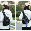A woman wearing a white hoodie and a beige hat is shown from behind carrying a black tactical fishing gear storage chest bag.
