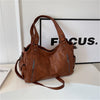Un sac fourre-tout en cuir marron avec une poignée et plusieurs poches zippées, exposé sur une surface blanche.