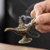 A hand holds an antique metal incense burner, releasing smoke against a dark background.