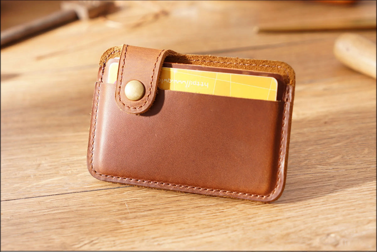 Porta tarjetas delgado de cuero genuino marrón con una tarjeta dorada insertada sobre una superficie de madera.
