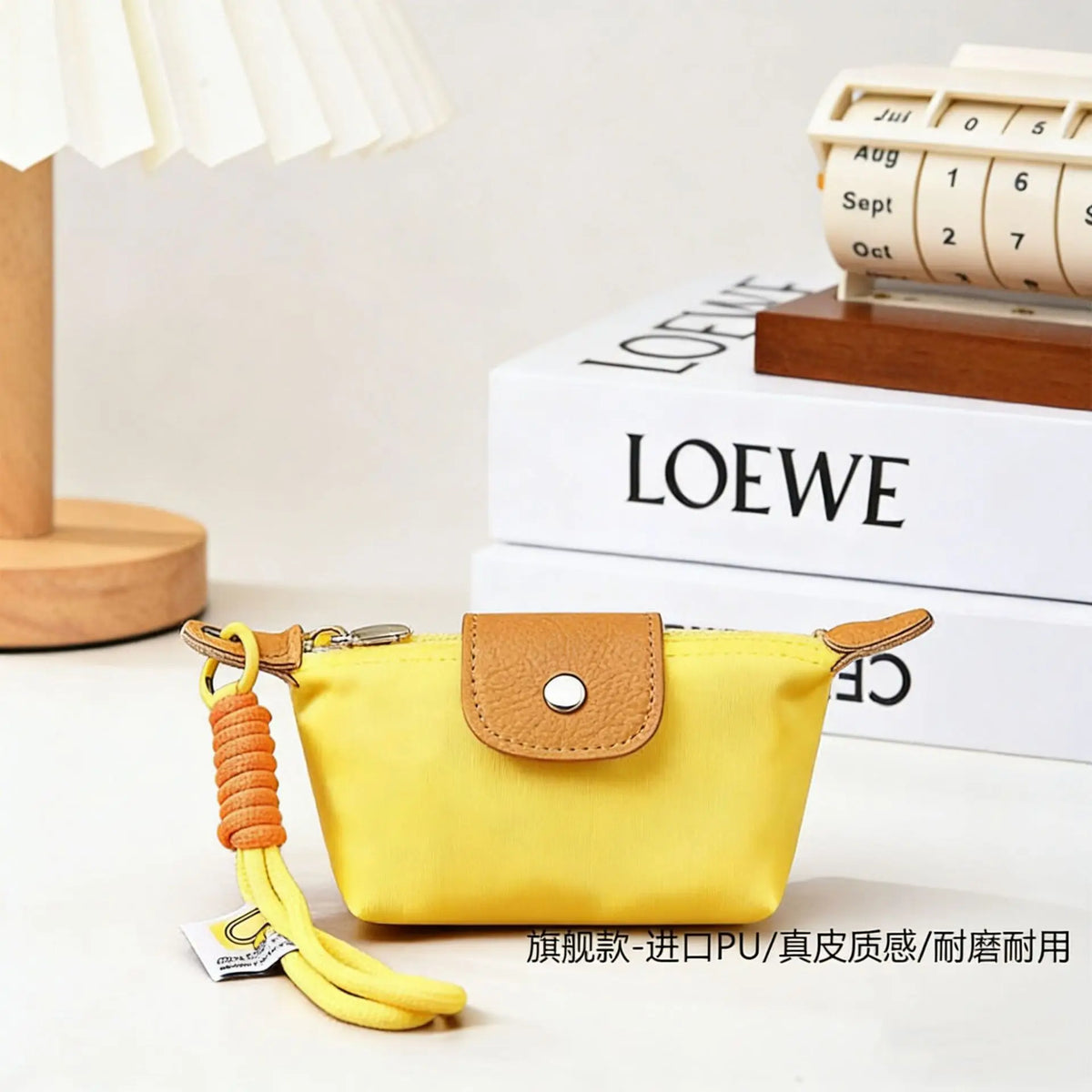 A yellow compact coin purse with a leather flap and keychain strap resting on a white surface next to stacked books.