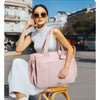A woman wearing a white top and skirt sits on a yellow chair outdoors while holding a pink large capacity tote bag.