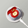 A white ceramic dish holds a red fruit-shaped earphone case with a yellow center and green accents.