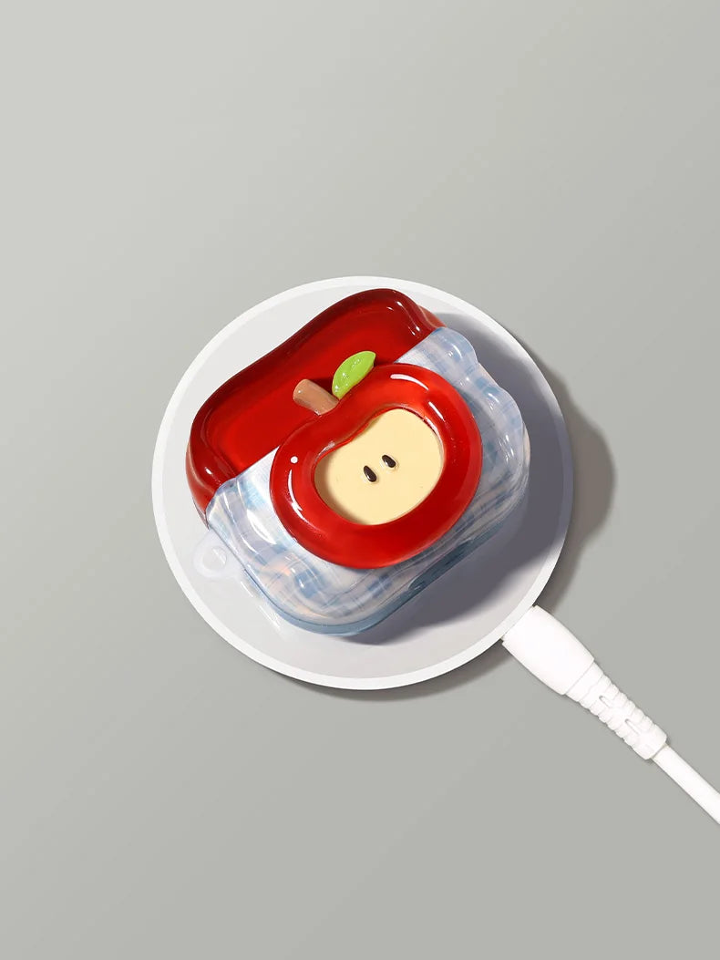A white ceramic dish holds a red fruit-shaped earphone case with a yellow center and green accents.