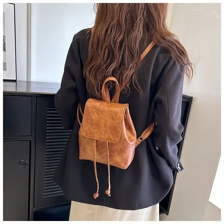 Une femme tient un mini sac à dos de type string rétro marron sur un fond clair.