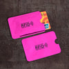 Two pink anti-scan card sleeves for RFID protection are displayed on a dark surface.