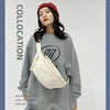 A woman models a light beige corduroy waist pack and a gray sweatshirt with a red beanie.