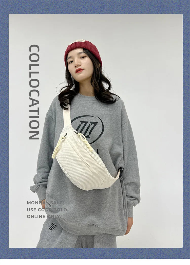 A woman models a light beige corduroy waist pack and a gray sweatshirt with a red beanie.