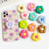 A collection of colorful, flower-shaped silicone phone grips and ring stands arranged on a white surface.