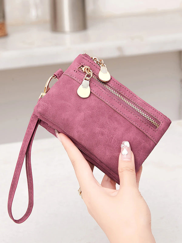 A hand holds a mauve retro PU leather double fold wallet with gold zipper pulls.