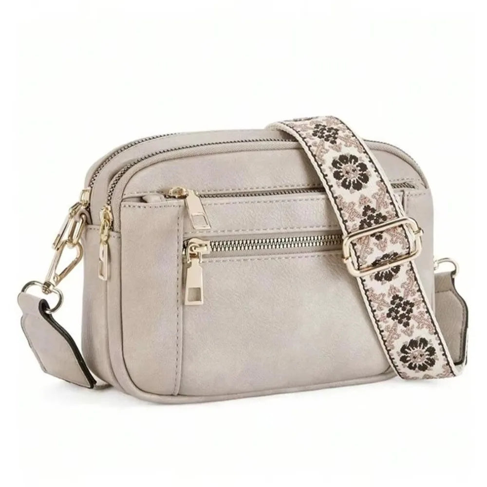A light gray retro square crossbody bag with a patterned strap and gold hardware.