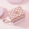 A light pink elegant letter zipper wristlet wallet with gold hardware resting on a white surface.