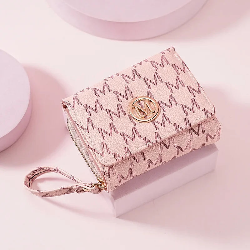 A light pink elegant letter zipper wristlet wallet with gold hardware resting on a white surface.