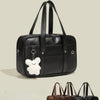 Black waterproof PU leather student messenger bag with a white bear charm shown from the side.