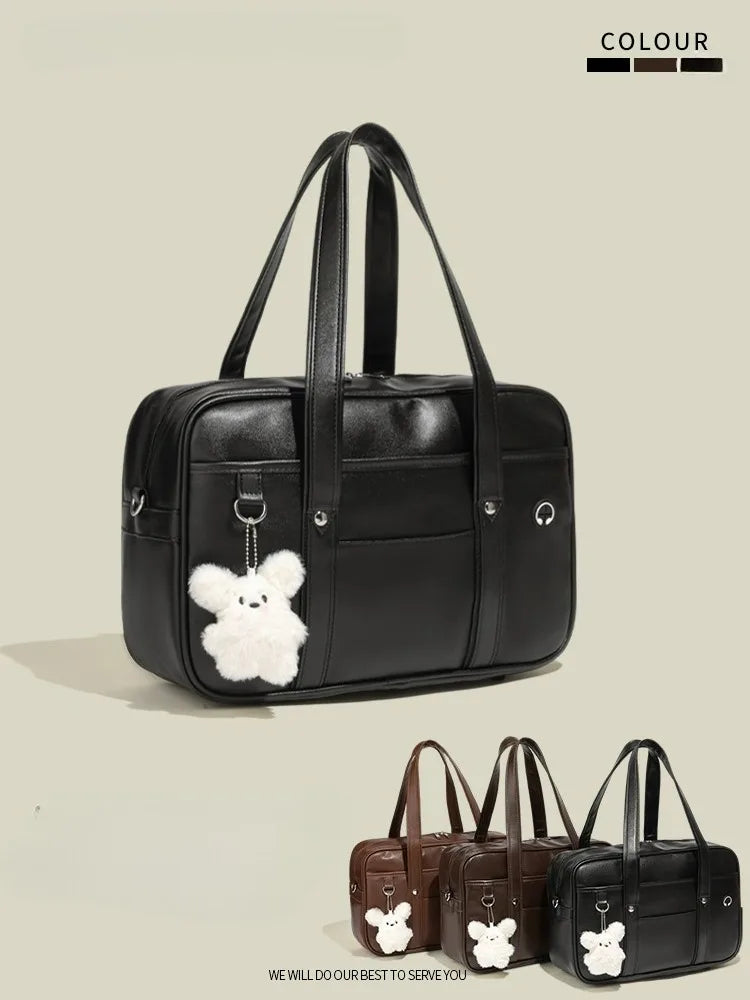 Black waterproof PU leather student messenger bag with a white bear charm shown from the side.