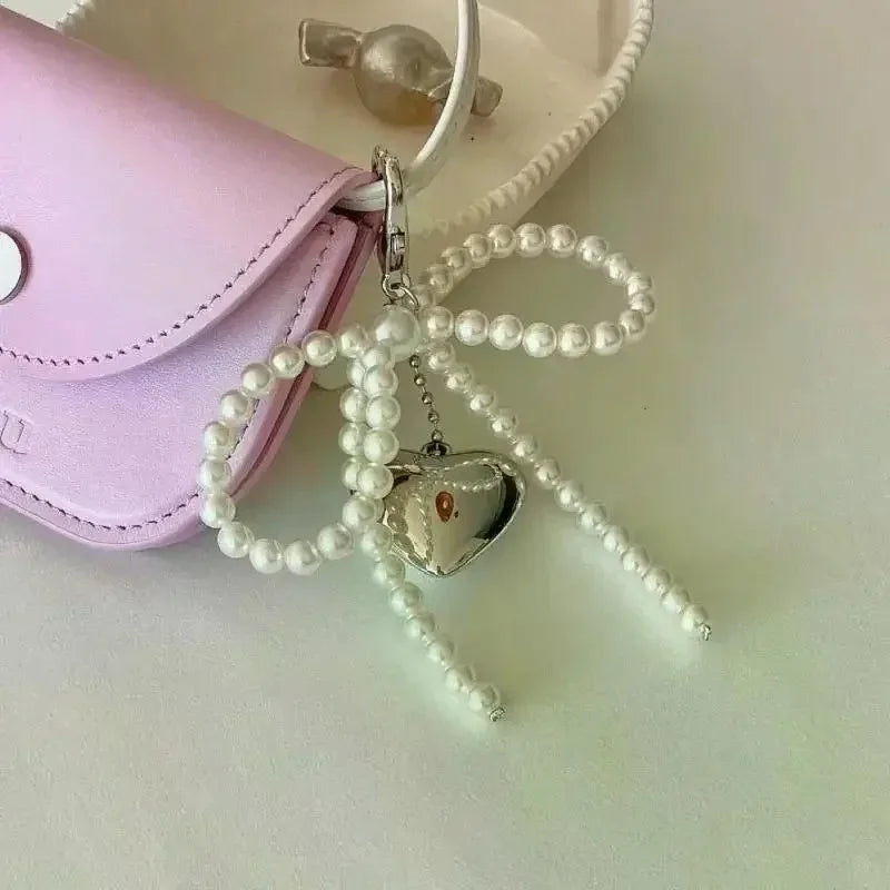 A pearl bow keychain with a heart pendant is displayed next to a light purple leather pouch.