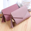 A light pink waterproof nylon crossbody bag with gold-toned tassels resting on a wooden surface.
