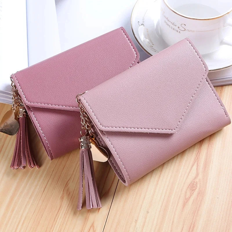 A light pink waterproof nylon crossbody bag with gold-toned tassels resting on a wooden surface.