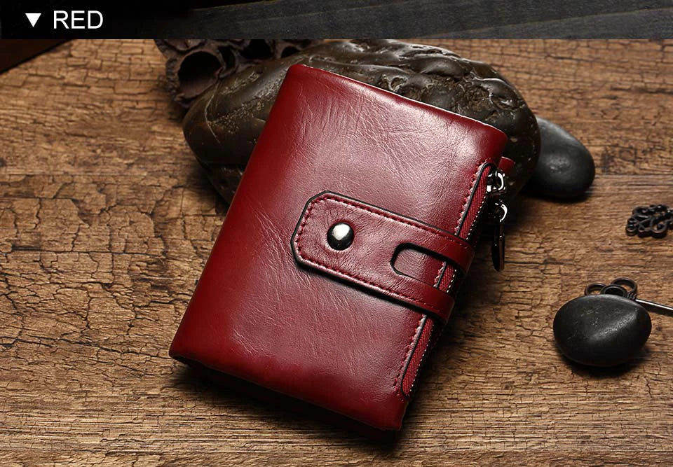 Ein tiefrotes, echtes Leder-Zweisefalldertasche auf einer Holzoberfläche neben dunklen Steinen.