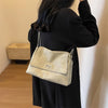 Una mujer sostiene un bolso de hombro de cuero retro beige contra una pared blanca.