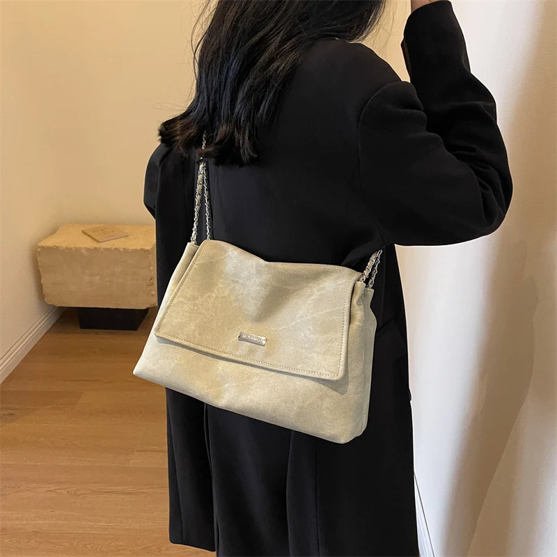 Una mujer sostiene un bolso de hombro de cuero retro beige contra una pared blanca.