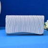 A light blue satin evening clutch with vertical pleats and a chain strap resting on a blue surface.