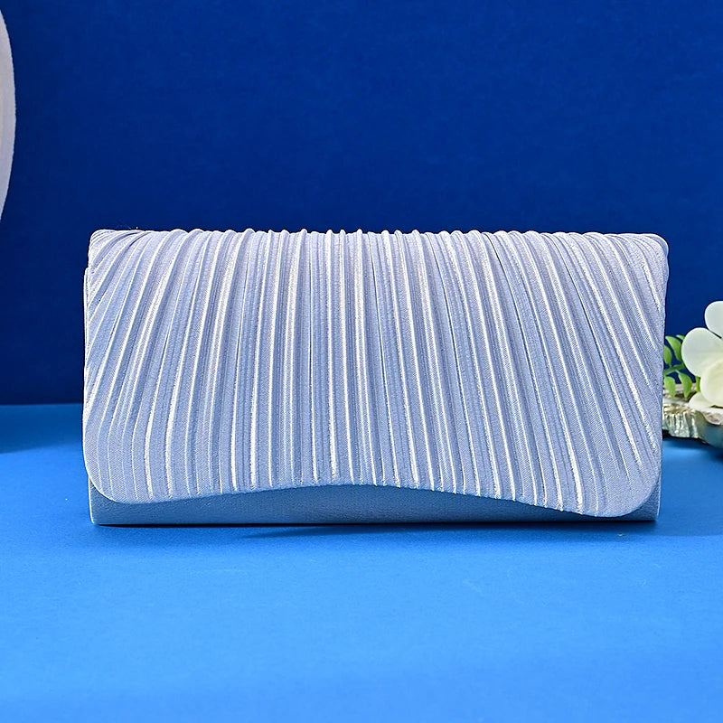 A light blue satin evening clutch with vertical pleats and a chain strap resting on a blue surface.