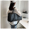 A person is holding a black crocodile grain PU leather travel duffle bag in front of white slatted blinds.