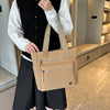 A person holds a tan canvas tote bag in front of a modern bookshelf interior.