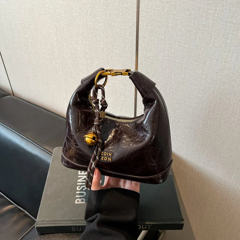 A dark brown retro PU leather shoulder bag with gold hardware is held by a hand against a gray background.