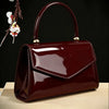 A glossy dark burgundy evening handbag with a gold hardware resting on a light wooden surface.