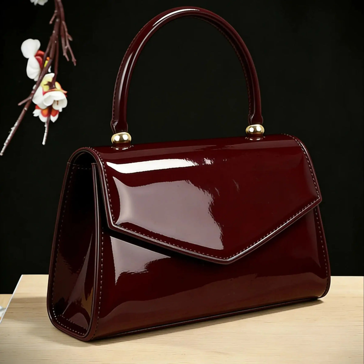 A glossy dark burgundy evening handbag with a gold hardware resting on a light wooden surface.