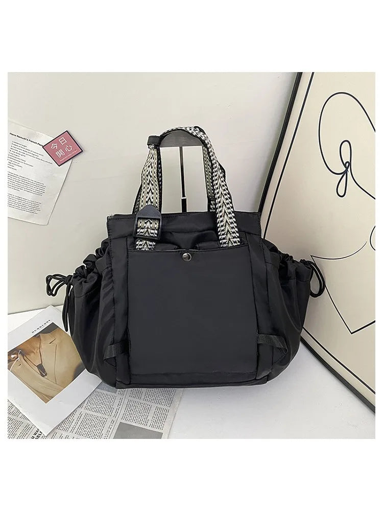 A black nylon shoulder bag with a striped handle and flap is displayed against a light background.