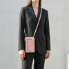 Eine Frau in einem dunkelgrauen Blazer und Hosen, die eine pinke Touchscreen-Crossbody-Handytasche trägt.