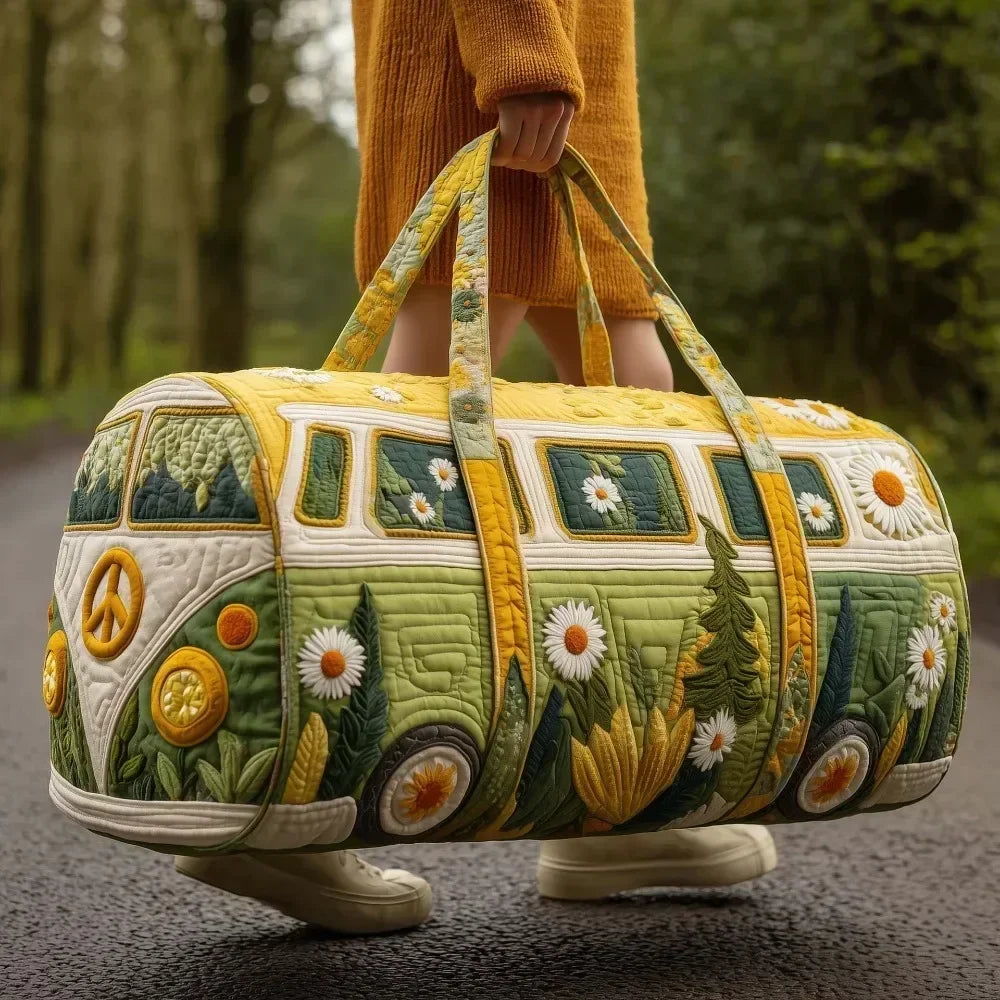 A yellow quilted travel duffle bag decorated with floral and foliage embroidery, held by a person in an orange sweater.