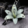 A realistic pale green phalaenopsis orchid flower keychain attached to a black leather backpack.